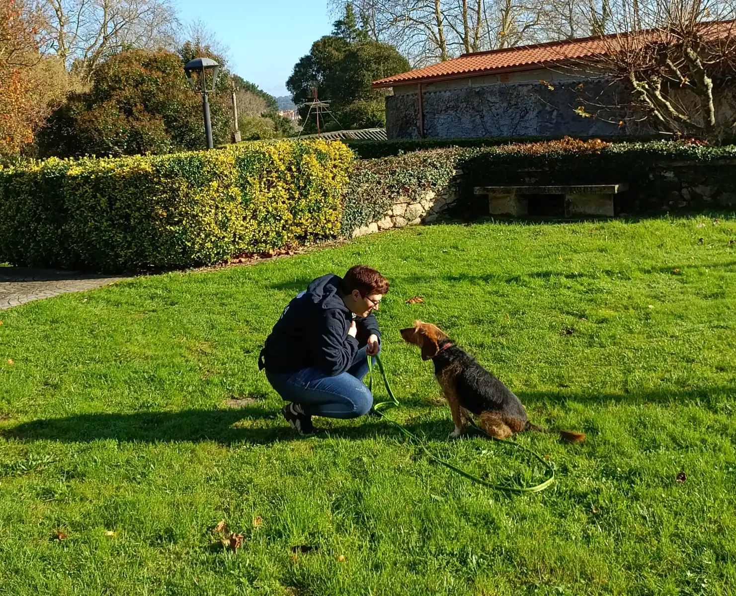 Mari mantiene la atención en su guía durante un ejercicio de trabajo en exterior, en un entorno tranquilo y verde.